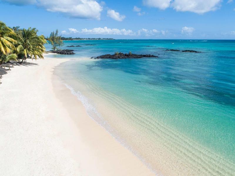 Ein weißer Sandstrand mit Palmen und klarem türkisfarbenem Wasser unter blauem Himmel.