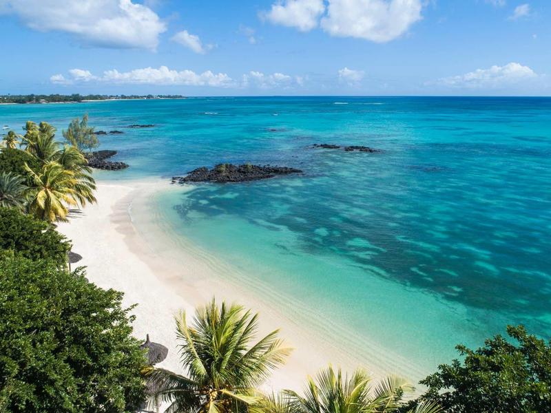 Weißer Sandstrand mit grünen Palmen und türkisfarbenem, klarem Meer unter blauem Himmel.