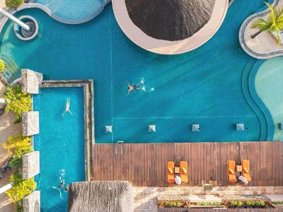 Luchtfoto van een tropisch hotelzwembad met ligstoelen en palmbomen.