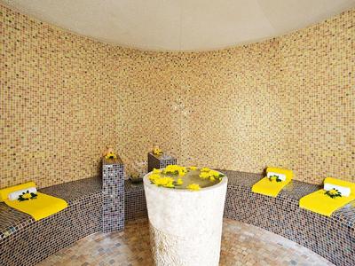 Interiér hammamu s mozaikovými kamennými stěnami a žlutými ručníky na lavičkách.