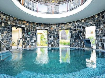 Kruhový krytý bazén s hladkou modrou mozaikou a přírodní kamennou zdí pod velkým světlíkem.