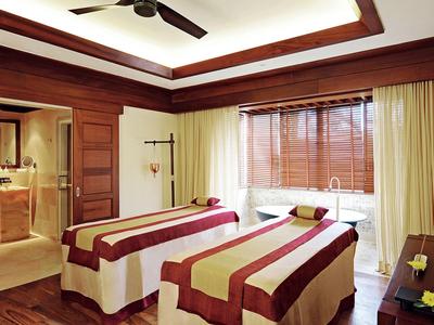 Moderní spa místnost se dvěma masážními stoly, teplým osvětlením a dřevěnými prvky.