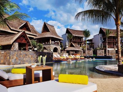 Luxusní resortní vily s bazénem, obklopené palmami a modrou oblohou.