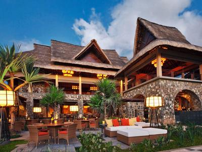 Velký tropický resort s dřevěnou střechou a útulným venkovním posezením za soumraku.