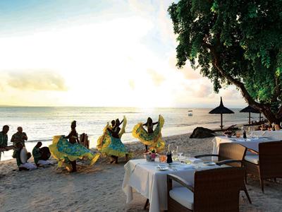 Dansers voeren een traditionele show uit op het strand bij zonsondergang, tafels klaar voor diner.