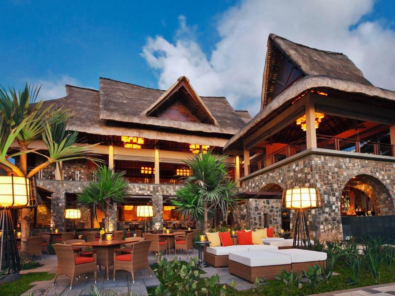 Luxusní tropické středisko s designem ze dřeva a kamene, venkovními lehátky a osvětlenou zahradou.