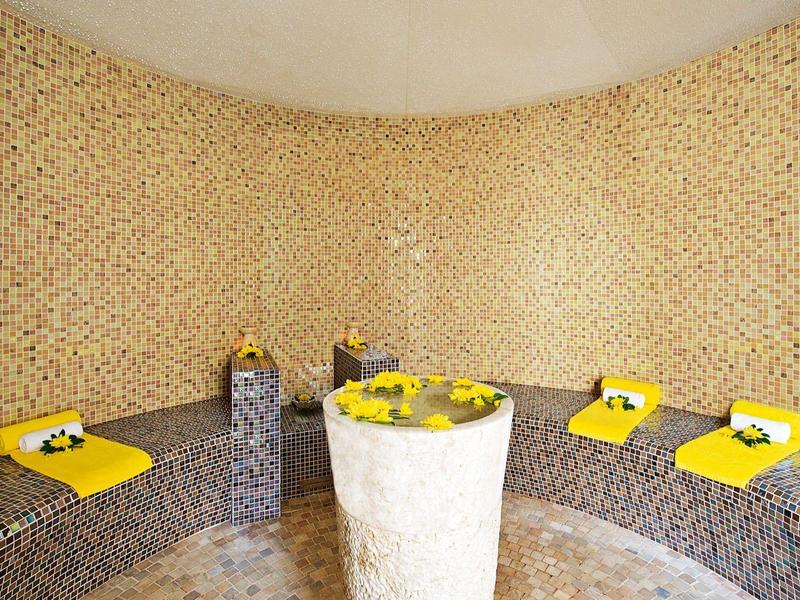 Interiér hammamu s mozaikovými kamennými stěnami a žlutými ručníky na lavičkách.