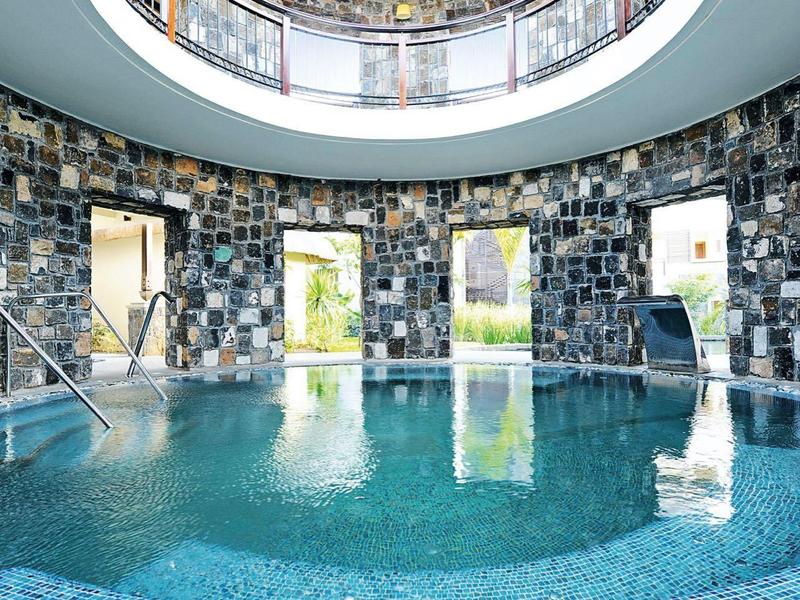 Kruhový krytý bazén s hladkou modrou mozaikou a přírodní kamennou zdí pod velkým světlíkem.
