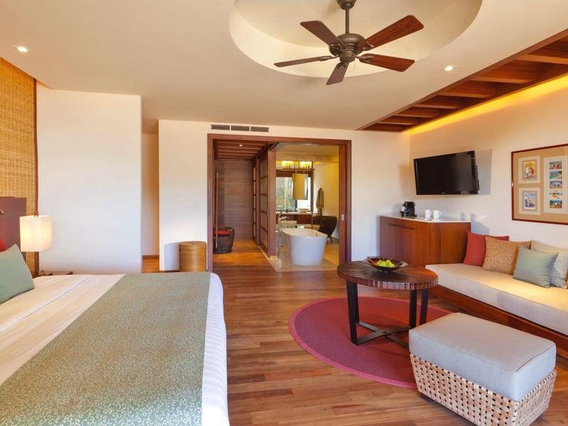 Elegantní hotelový pokoj s posezením, stropním ventilátorem a volně stojící vanou.