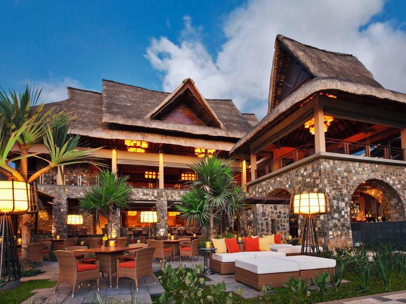 Velký tropický resort s dřevěnou střechou a útulným venkovním posezením za soumraku.