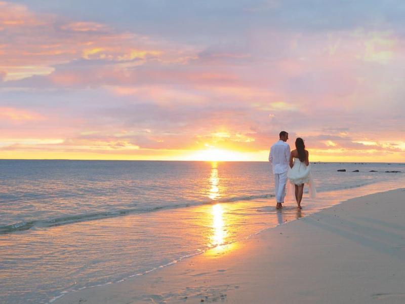 Pár prochází klidnou pláží během barevného západu slunce.