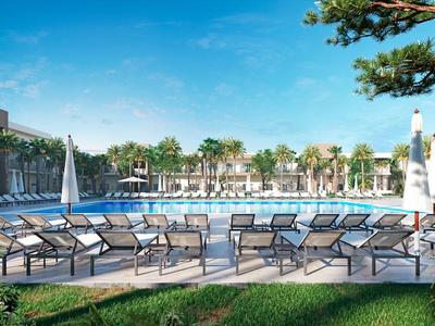 Moderner Hotelpool mit Liegestühlen und Blick auf Palmen unter blauem Himmel.