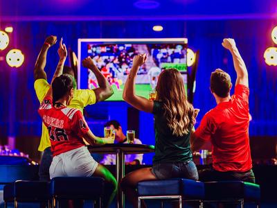 Gruppo che festeggia davanti a una TV in un bar con illuminazione atmosferica.