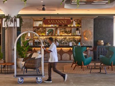 Hotelpersonal schiebt Gepäckwagen durch einen eleganten Hotel-Lobbybereich mit Bar