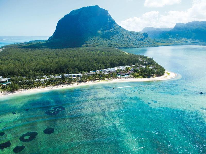 Türkisfarbenes Meer mit Sandstrand und bewaldetem Berghang im Hintergrund