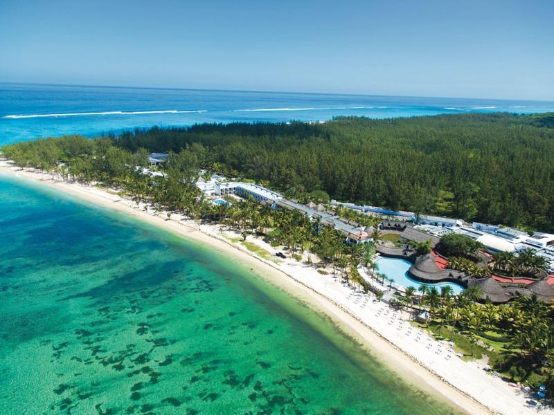 Luftaufnahme eines tropischen Strandes mit klarem Wasser, grünen Bäumen und Resortgebäuden.
