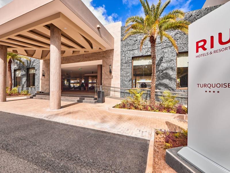 Eingangsbereich eines Hotels mit Säulen, Palmen und klarem Himmel