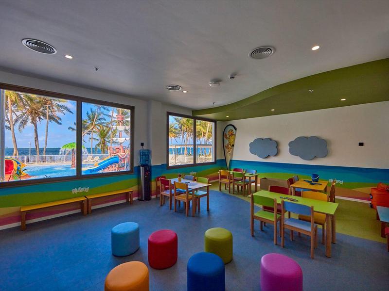 Bunter Kinderspielraum mit Sitzwürfeln, Tischen und Blick aufs Meer durch große Fenster