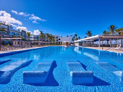 Großer Außenpool mit Sonnenliegen und Palmen unter klarem blauem Himmel in einem Hotelresort.