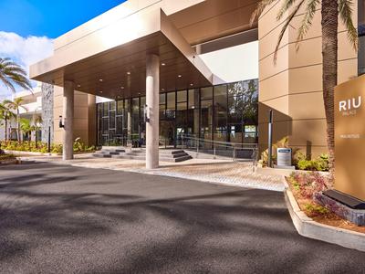 Moderner Hoteleingang mit großem Vordach, Säulen und Palmen in heller Umgebung.