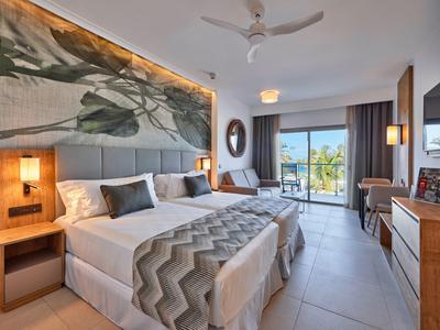 Modernes Hotelzimmer mit zwei Betten, Holzdekor und Blick auf einen Balkon mit Meerblick.