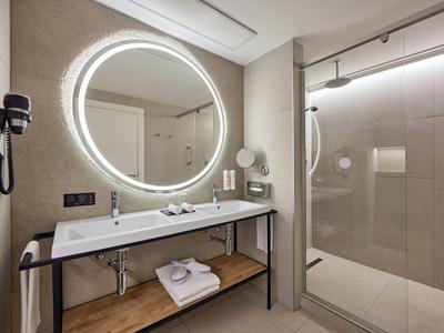 Modernes Badezimmer mit beleuchtetem Spiegel, waschbecken, Haartrockner und regendusche