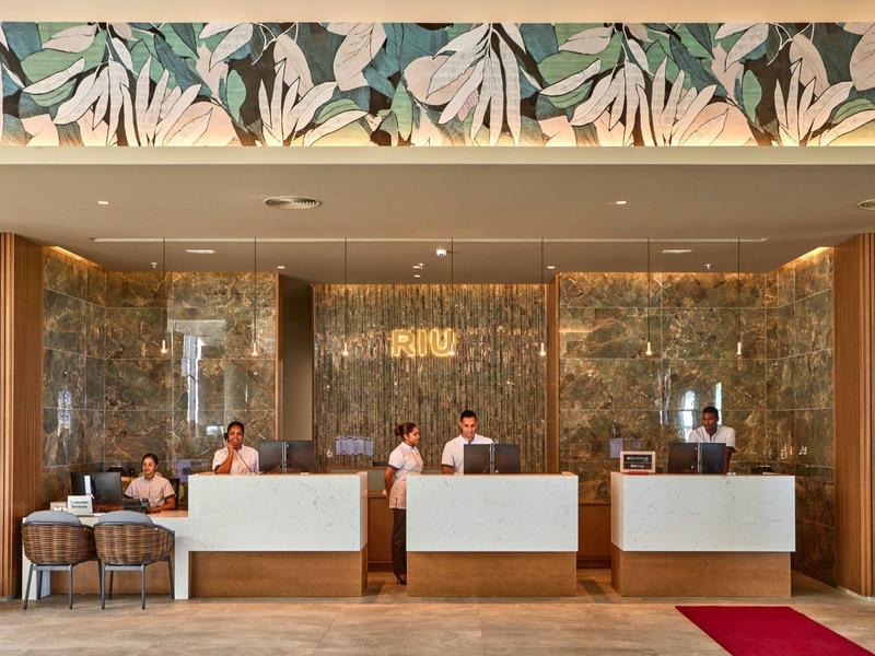 Hotelrezeption mit drei Schaltern, Mitarbeitern und Gästen in einem modernen Empfangsbereich.