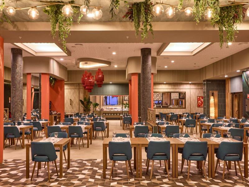 Großer Speisesaal mit blauen Stühlen, dekorierter Decke und warmem Licht.