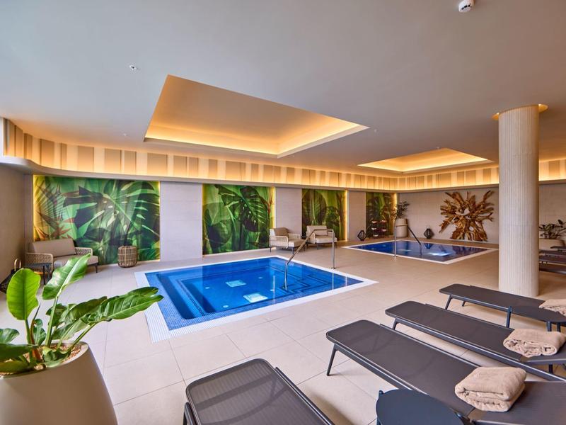 Moderner Innenpoolbereich mit Liegestühlen, großen Pflanzen und beruhigender Beleuchtung.