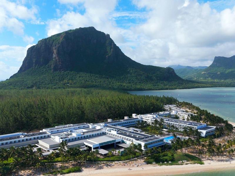 Resort am Strand mit Blick auf einen markanten Berg unter blauem Himmel mit Wolken.