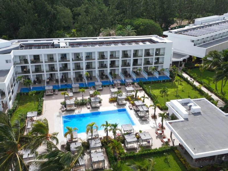 Moderner Hotelkomplex mit Swimmingpool, Liegestühlen und grüner Umgebung bei sonnigem Wetter.