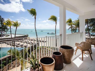 Balkon mit Stühlen und Töpfen mit Meerblick und Palmen unter blauem Himmel.