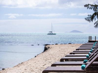 Leere Liegestühle stehen am sandigen Strand mit Blick auf das Meer und ein Segelboot.