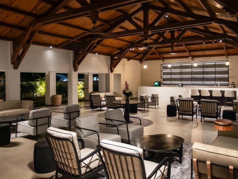 Großer Lounge-Bereich mit Holzdecke, Metallstühlen, Tischen und Bar am rechten Rand.