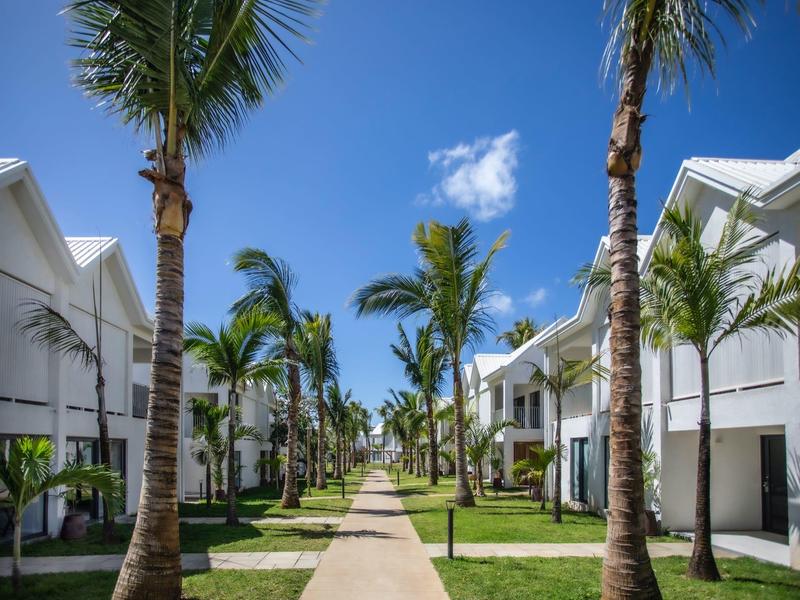 Moderner Wohnweg zwischen weißen Häusern mit Palmen und blauem Himmel.