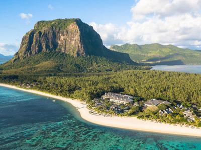 Tropical resort on white sandy beach with mountain and sea in the background.