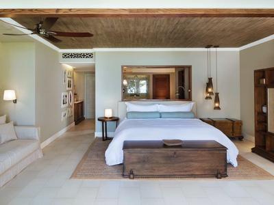 Bright hotel room with large bed, sofa, mirror, and wooden furniture.