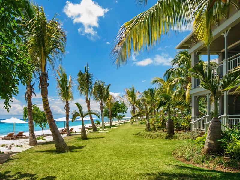 View of a tropical beach with palm trees and a resort under a blue sky.
