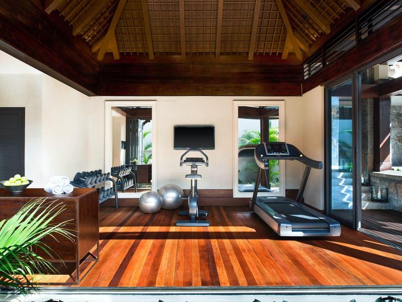 Modern gym with wooden floor, treadmill, exercise bike, and large windows overlooking greenery.