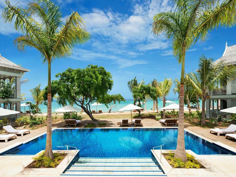 Luxurious pool area with palm trees, sun loungers, and ocean view at the beach.