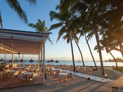 Beachside open-air restaurant with palm trees and sunset over the sea.
