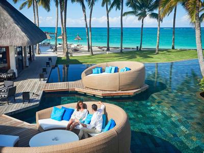 Paar genießt entspannte Zeit in runder Lounge am Pool mit Blick auf Meer und Palmen.