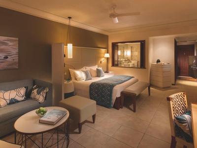 Elegant hotel room with double bed, sofa, tables, and stylish lighting.