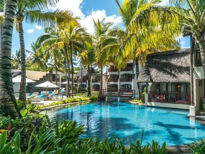 Hotel pool with palm trees and sun loungers in front of a multi-story building on a sunny day.
