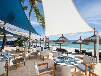 Bright beach restaurant with tables, chairs, sun sails, overlooking the sea and palm trees.