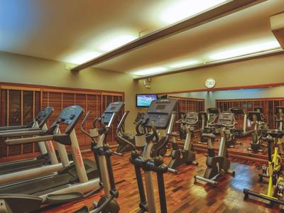 Fitnessraum mit mehreren Laufbändern und Fahrrädern, Holzboden und heller Beleuchtung.