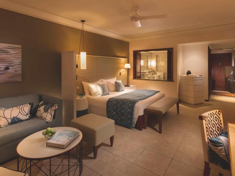 Elegant hotel room with double bed, sofa, tables, and stylish lighting.