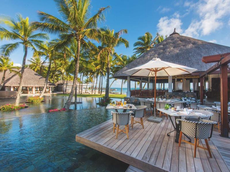 Outdoor restaurant with tables and chairs beside a pool and palm trees at a tropical resort.
