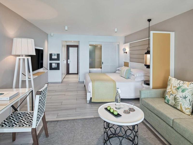 Bright, modern hotel room with seating area, desk, and double bed