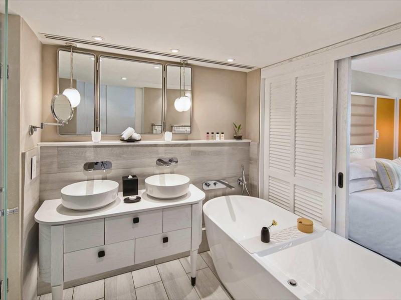 Modern bathroom with double sinks, freestanding bathtub, and access to the bedroom.